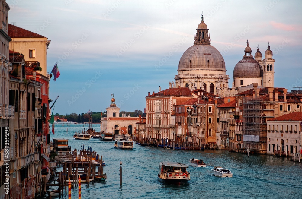 Romantic scenery of Venice bathed in dusk rosy light, with boats & ferries cruising on Grand Canal and landmark cathedral Basilica Santa Maria della Salute in background, an amazing city in Italy
