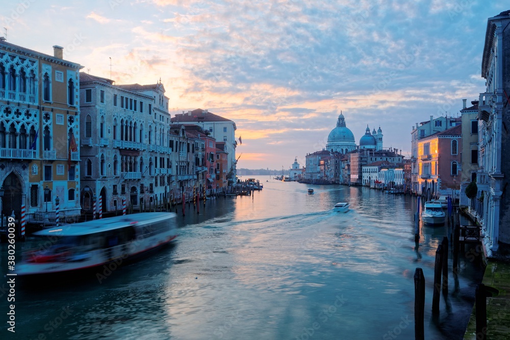 Morning scenery of the Grand Canal bathed in golden twilight, with boats & ferries cruising on waterway & landmark cathedral Basilica Santa Maria della Salute in background, in romantic Venice, Italy
