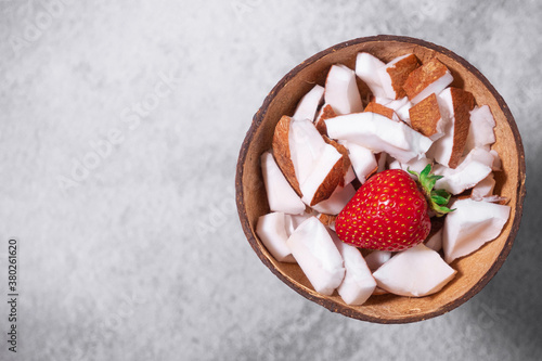 A bowl of coconut pieces and strawberry on concrete background. Coconut ingredient on plate. Vegan organic snack in zero waste coconut bowl. Space for text. Place for text. Banner for vegan cafe
