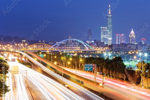Nightscape of Taipei City with Taipei 101 Tower among skyscrapers in XinYi District downtown, beautiful arch bridges & busy car trails on riverside avenue ~ Scenery of prosperous Taipei in twilight