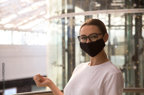 Beautiful caucasian girl in a black protective mask in a shopping mall with shopping bags. New normal portrait © svitlini
