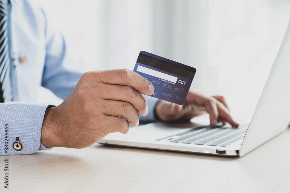 Fototapeta premium The businessman's hand is holding a credit card and using a laptop for online shopping and internet payment in the office