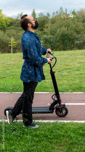 man with a mask walks thoughtfully with his electric scooter