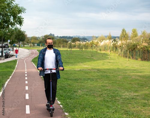 man with a mask drives electric scooter on a bike lane