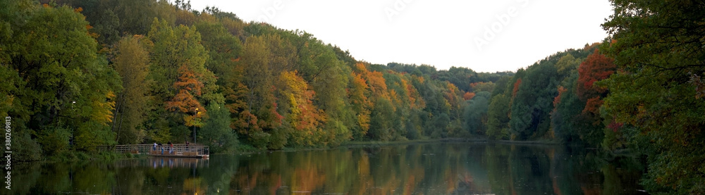 Panoramic view of evening autumn lake with colorful trees and first lanterns