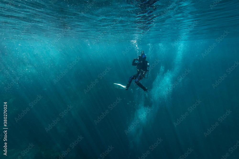 The diver begins the dive in the clear water, the sun's rays illuminate the background beautifully and bubbles rising. Very beautiful frame The diver begins the dive in the clear water, the sun's rays illuminate the background beautifully and bubbles rising. Very beautiful frame