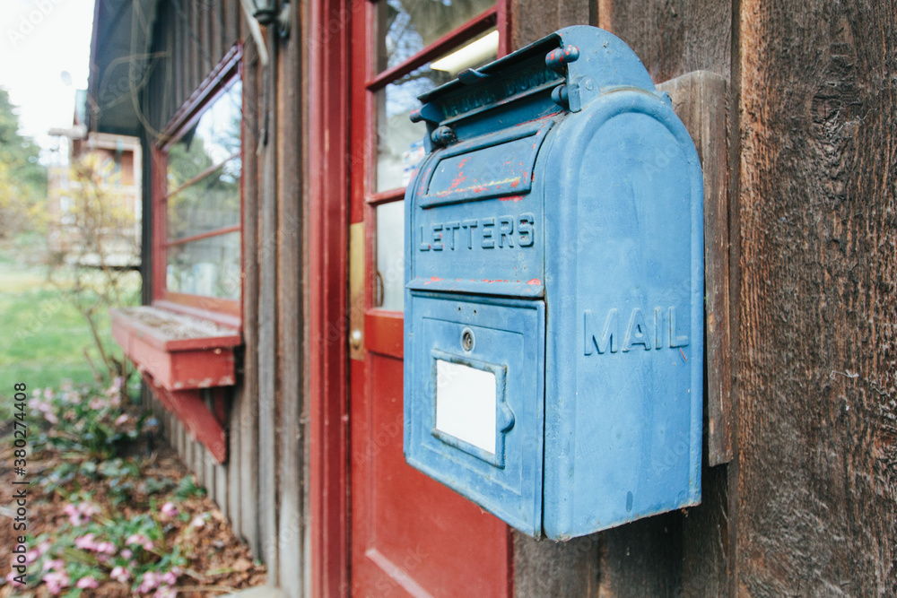 Old blue mailbox hanging on a wooden panel wall of a small, rustic building Old blue mailbox hanging on a wooden panel wall of a small, rustic building