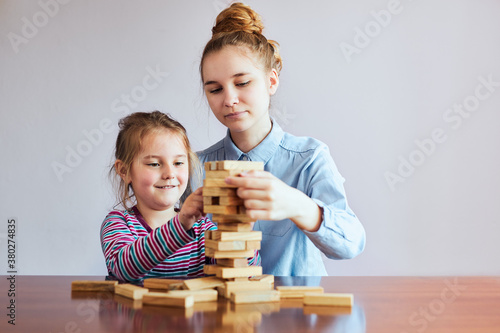 Little girl preschooler and her elder sister playing together with wooden blocks game toy. Siblings spending time sitting at desk at home