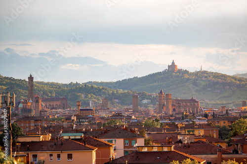 Aerial panoramic view of old Bologna city. It is saw Asinelli tower or torre, San Petronio church or basilica and San Luca church or basilica. Cloudy and sunset sky and bolognese hills in background