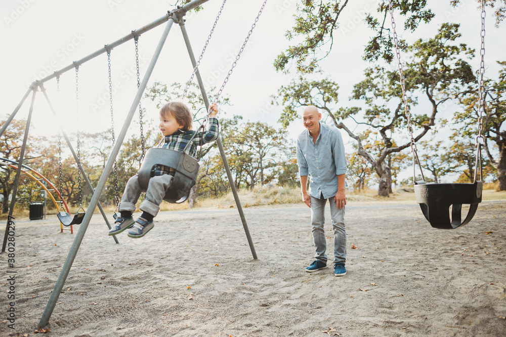Asian dad spending time with son outside - pushing him in swing Asian dad spending time with son outside - pushing him in swing