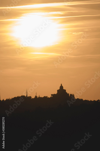 Panoramic view of San Luca Sanctuary at the sunset  with orange sky and sun in the background. There is the wood of the Bologna s hills   colli bolognesi . Emilia Romagna Region.