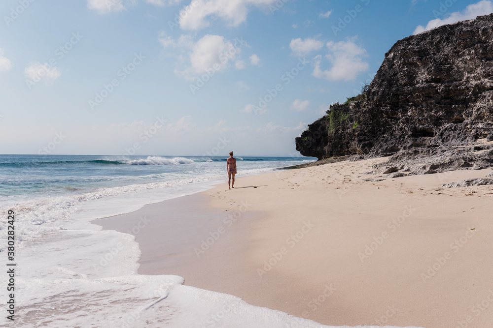 A woman walking on the white sand a sunny day - location is Dreamland Beach in Bali A woman walking on the white sand a sunny day - location is Dreamland Beach in Bali