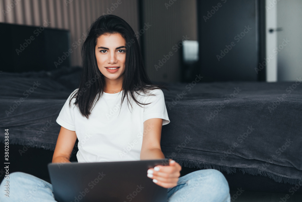 Beautiful young woman working on a laptop sitting on the floor near the bed Beautiful young woman working on a laptop sitting on the floor near the bed
