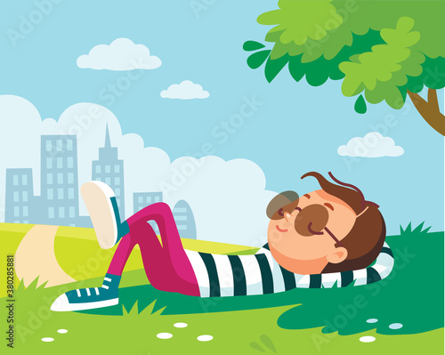 Portrait of a boy lying/resting/lies on green lawn in shade of tree in park, city outskirts. Summer.