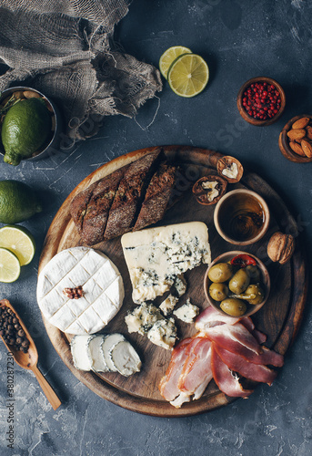 Set of cheese, hamon, honey, green olives, nuts and spices on rustic wooden board