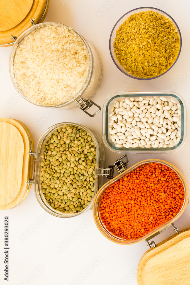 Uncooked dry cereal food group in glass containers on white,above view Uncooked dry cereal food group in glass containers on white,above view