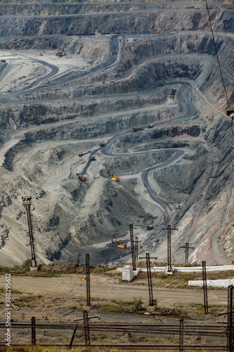 Giant iron ore quarry in Rudny,  Kazakhstan. Open pit mining raw minerals for steel production. Quarry machines, excavators and dump trucks and railroad on foreground. photo