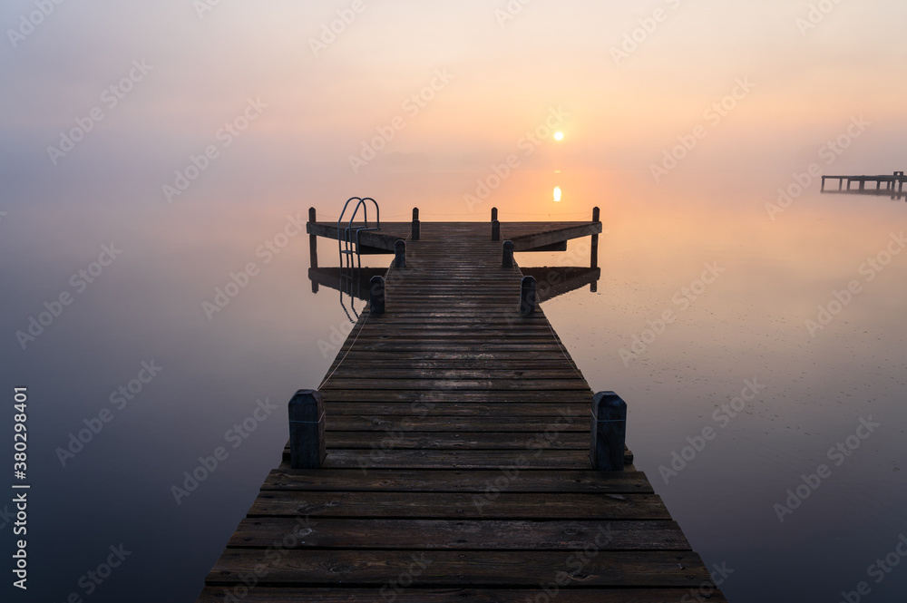 A jetty in a lake during a tranquil, foggy dawn.