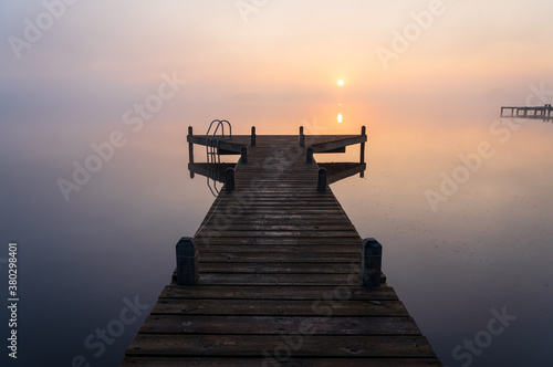 A jetty in a lake during a tranquil  foggy dawn.