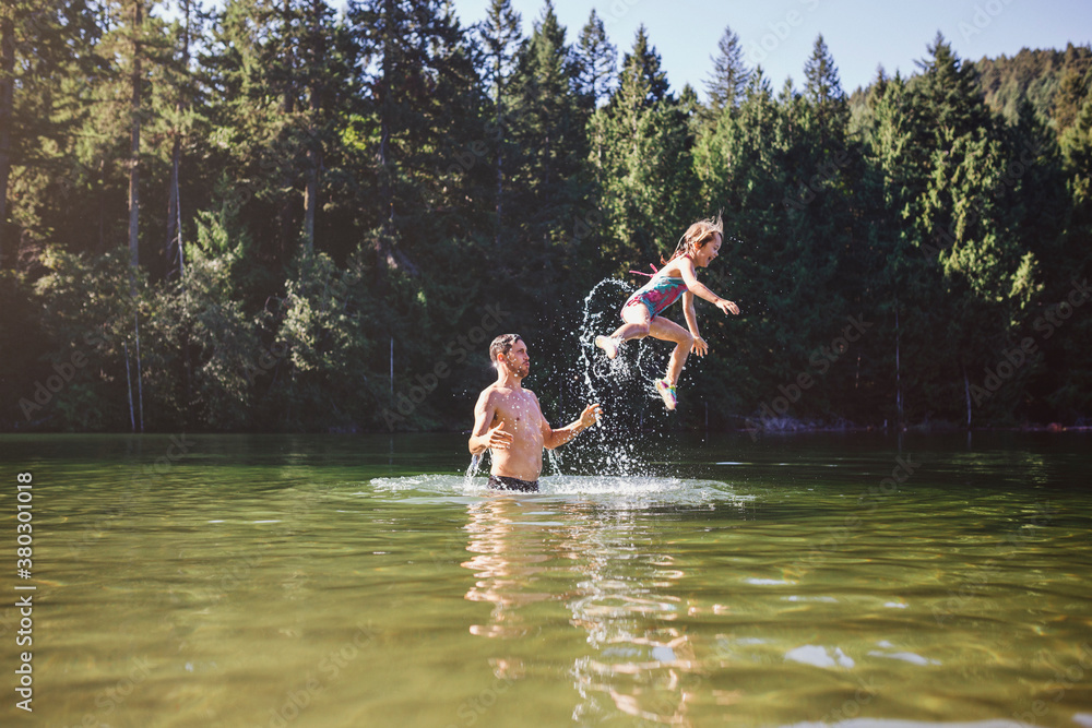 Young dad throwing daughter up and into the lake in summer - fun Young dad throwing daughter up and into the lake in summer - fun