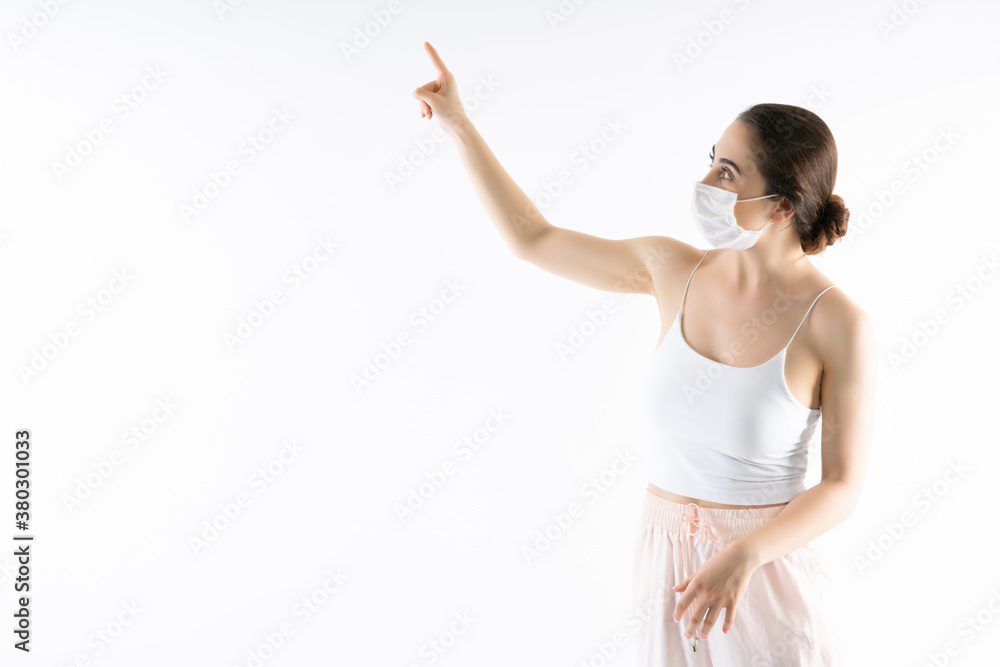Beautiful caucasian young woman in white t-shirt with disposable face mask. Protection versus viruses and infection.She is gesturing, copy space for your design Beautiful caucasian young woman in white t-shirt with disposable face mask. Protection versus viruses and infection.She is gesturing, copy space for your design