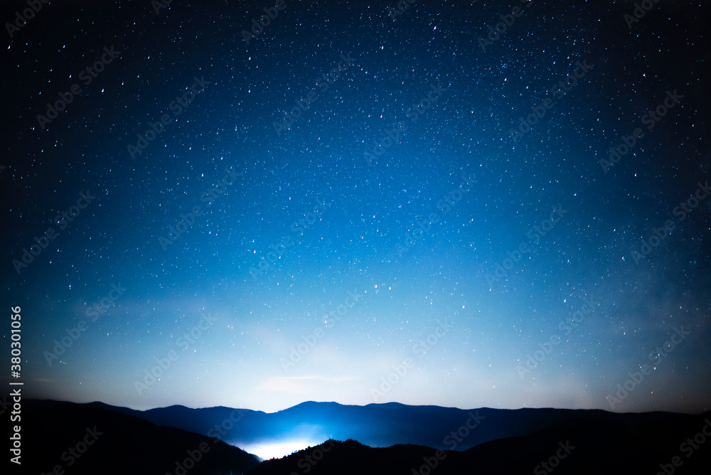 Starry sky over mountains panorama with city lights below