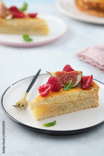 Piece of cheesecake with raspberries and figs on grey background.