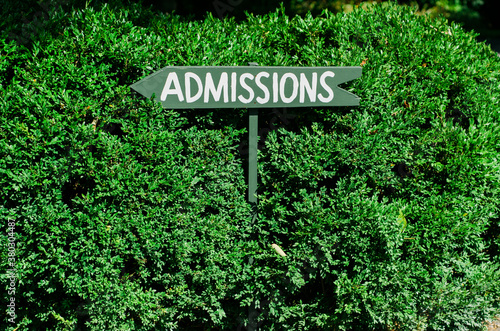 sign pointing to admissions against a green backdrop