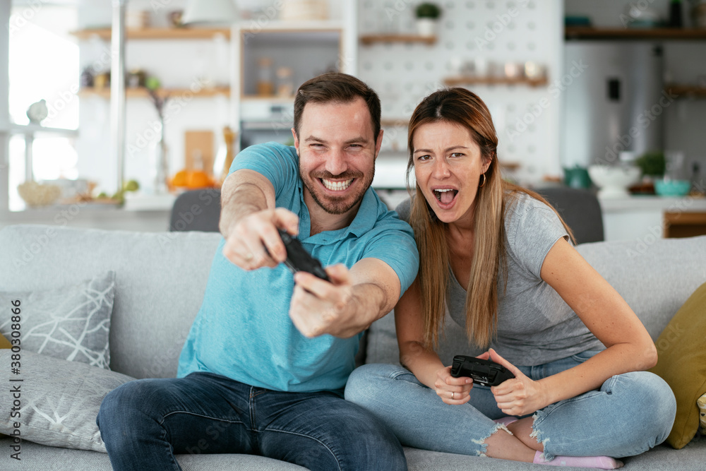 Boyfriend and girlfriend playing video game with joysticks in living room. Loving couple are playing video games at home.. Boyfriend and girlfriend playing video game with joysticks in living room. Loving couple are playing video games at home..