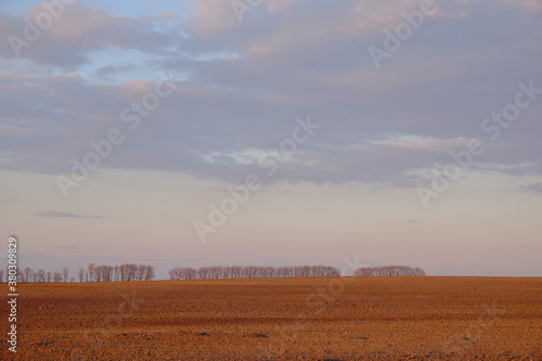 Cloudy evening sky over an empty agricultural field. Bright sunset landscape.