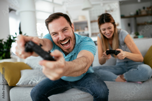 Boyfriend and girlfriend playing video game with joysticks in living room. Loving couple are playing video games at home..