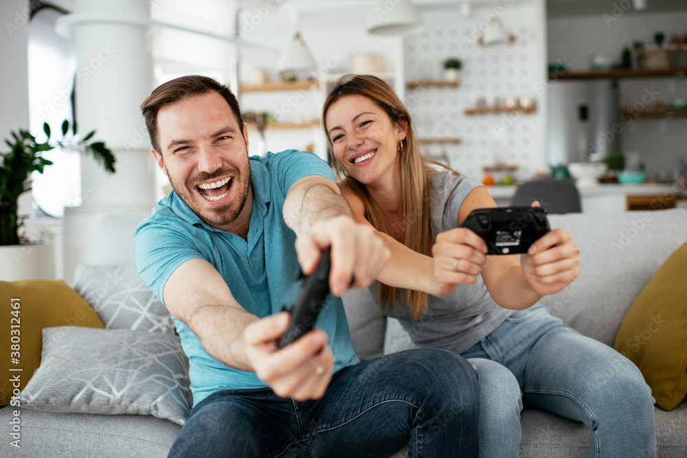 Boyfriend and girlfriend playing video game with joysticks in living room. Loving couple are playing video games at home.. Boyfriend and girlfriend playing video game with joysticks in living room. Loving couple are playing video games at home..