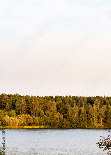 view of yellow and green forest on lake coast at autumn sunset photo