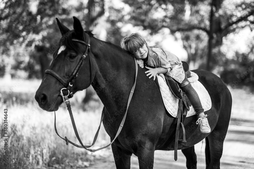 Obraz premium Cute little girl with long hair riding a horse outdoors. Pet therapy