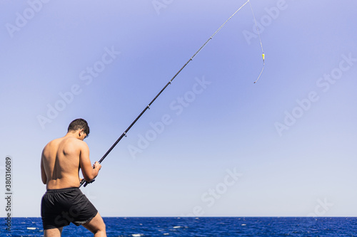 Young dark short-haired man of Maghreb origin fishing on his back, having a problems with a rod, with the fishing rod raised in the foreground.