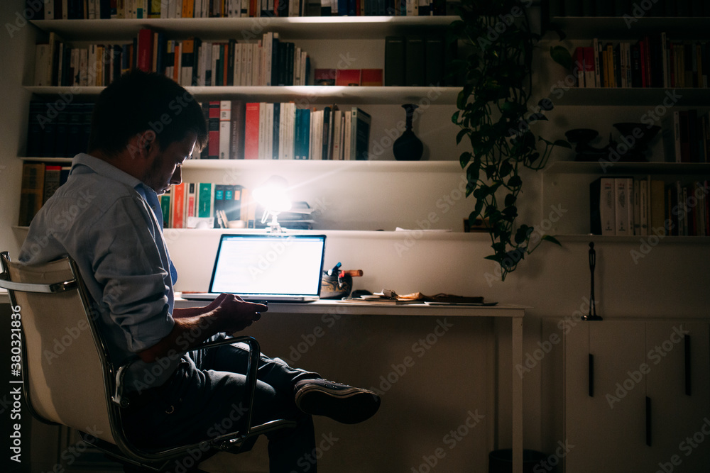 Man Reading Text Messages at His Desk at Night Man Reading Text Messages at His Desk at Night