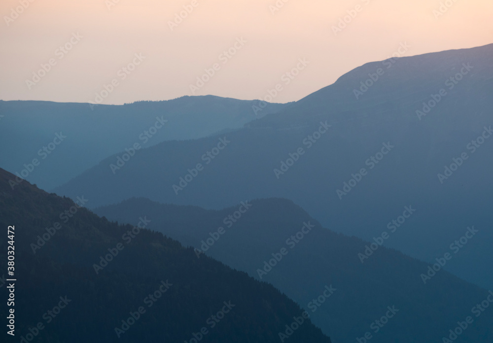 Silhouette of layered mountains ridge at sunset. Blue gradient background