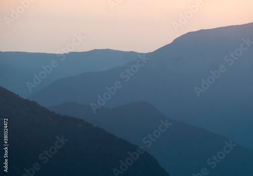 Silhouette of layered mountains ridge at sunset. Blue gradient background © lilkin