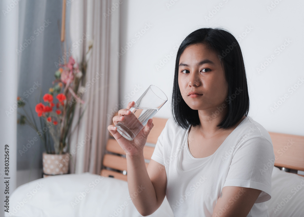 Beautiful Asian woman drinking fresh water from glass in white bedroom interior background Beautiful Asian woman drinking fresh water from glass in white bedroom interior background