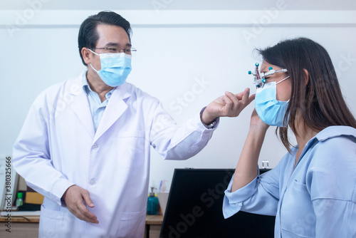 Asian woman wearing a protective mask with a trial frame to test her vision  optometrist in a protective mask takes care of her side
