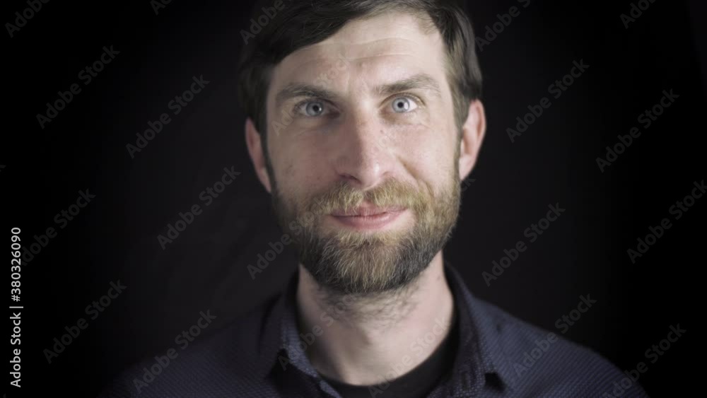 Portrait of a handsome man with a beard. Smiling at the camera, serious facial expression. Looks into the camera. Guy on a black background. Slow motion Portrait of a handsome man with a beard. Smiling at the camera, serious facial expression. Looks into the camera. Guy on a black background. Slow motion