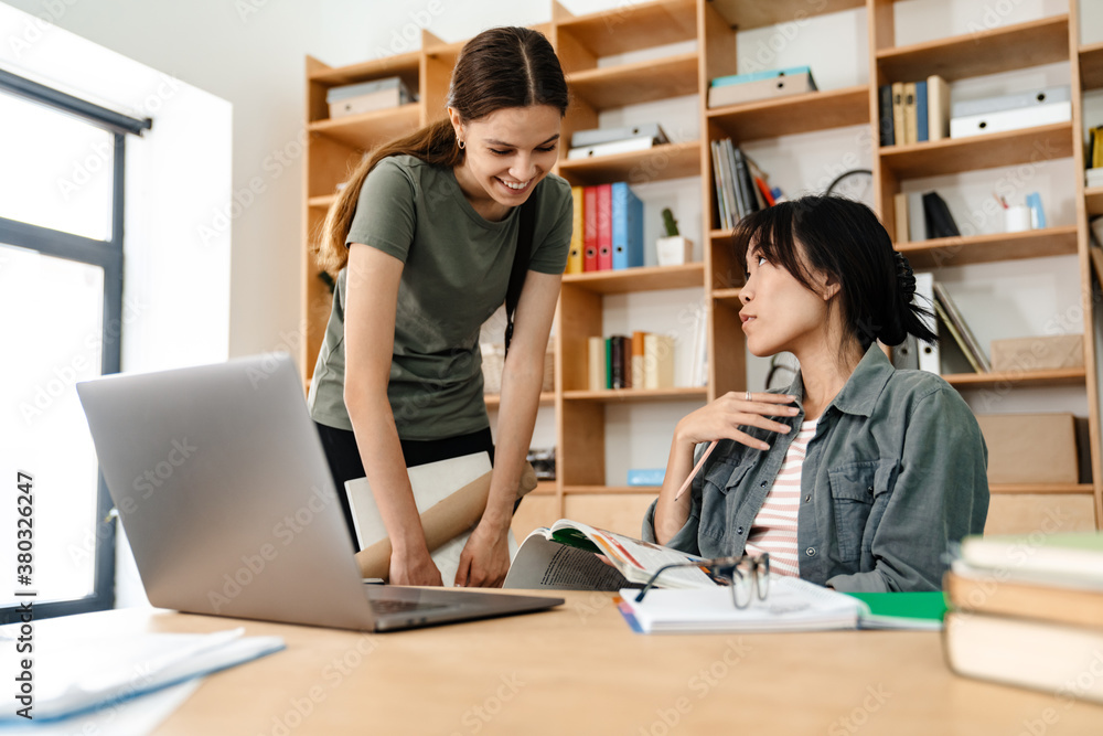 Photo of happy multinational students girls doing homework with laptop Photo of happy multinational students girls doing homework with laptop