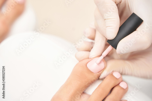 Beautiful salon procedure with pink pedicure on towel background. For decoration design. Healthcare. Woman body care. Spa treatment. White background. Nail brush paint. Apricot stick