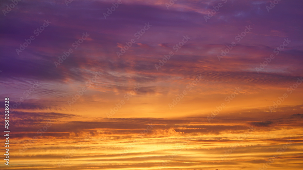 Blue sky with clouds at sunset. Sun rays through the clouds. Beautiful golden sunset. Orange yellow blue purple background.