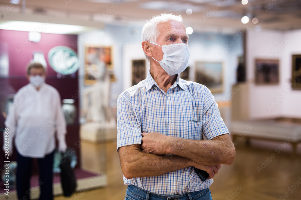 Obraz premium mature man in mask protecting against covid examines paintings on display in hall of art museum