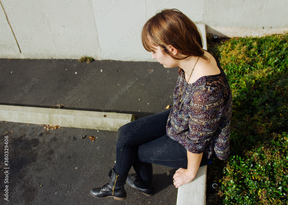 Young woman sits in sunny parking lot Young woman sits in sunny parking lot