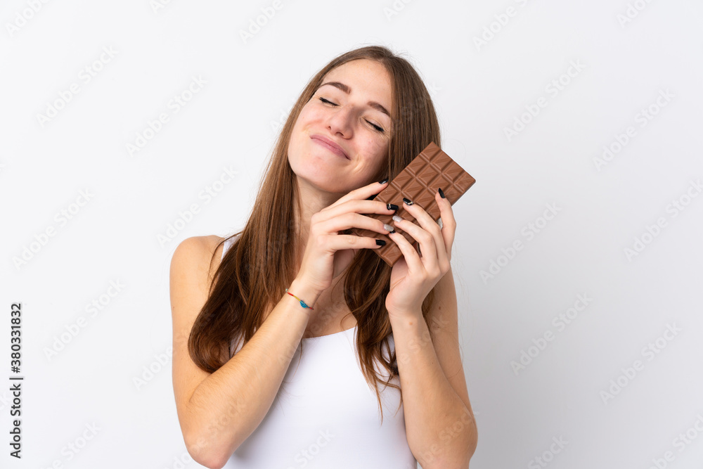 Young woman over isolated white background taking a chocolate tablet and happy Young woman over isolated white background taking a chocolate tablet and happy