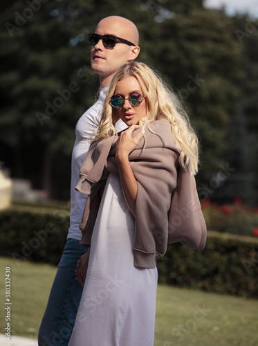 Stilish couple walking in modern clothers holding the hands each other, in sunglasses on autumn city background in the park. Closeup
