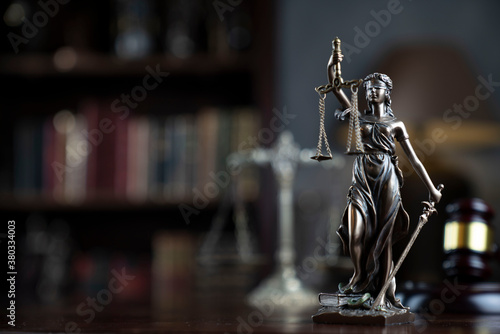 Law theme. Judge chamber. Themis, gavel and scale on brown shining desk. Collection of legal books in the bookshelf.