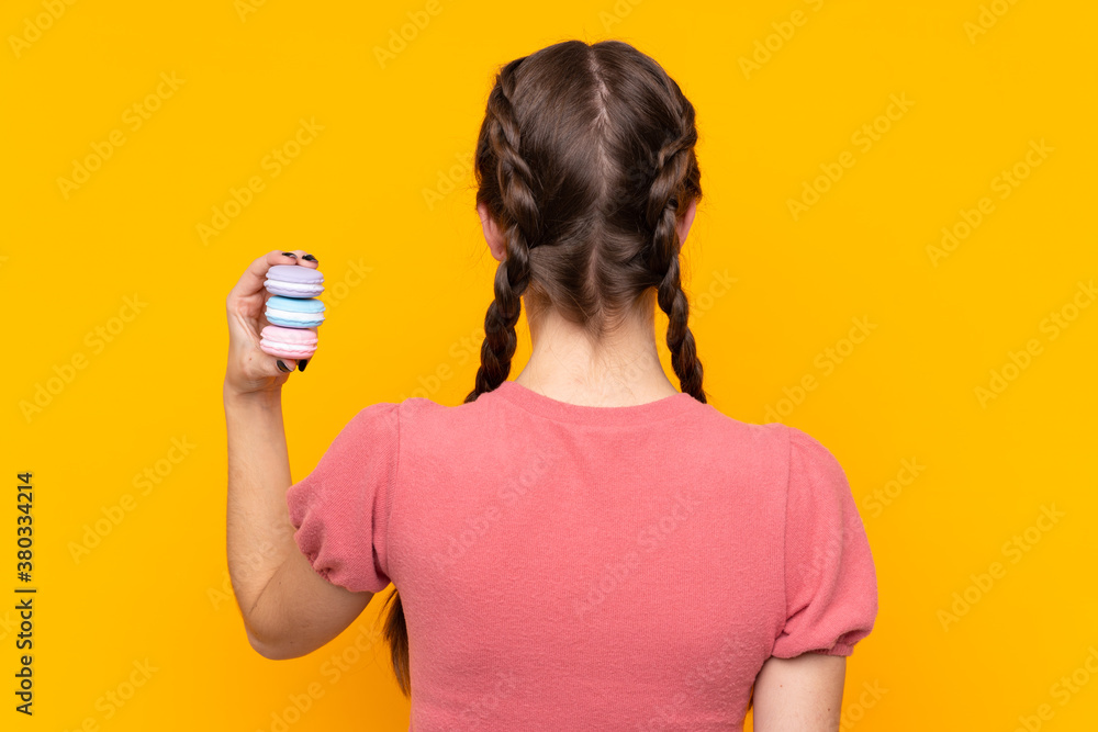 Young woman over isolated yellow background holding colorful French macarons Young woman over isolated yellow background holding colorful French macarons